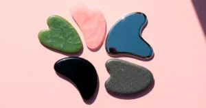 Piedras Gua Sha de jade, cuarzo rosa, obsidiana, acero inoxidable y piedra Bian sobre fondo rosa
